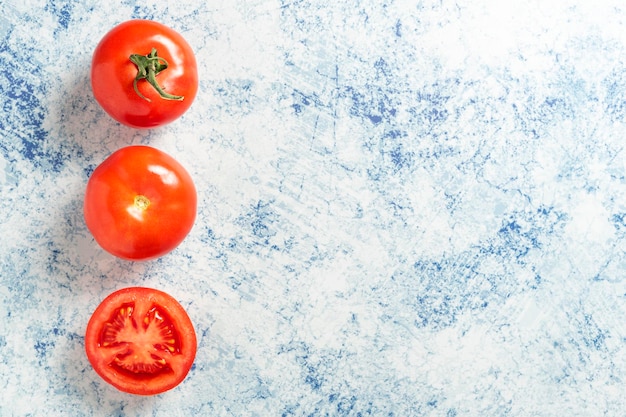 Tres tomates seguidos en una piedra azul Un tomate con tallo uno sin tallo y uno en rodajas