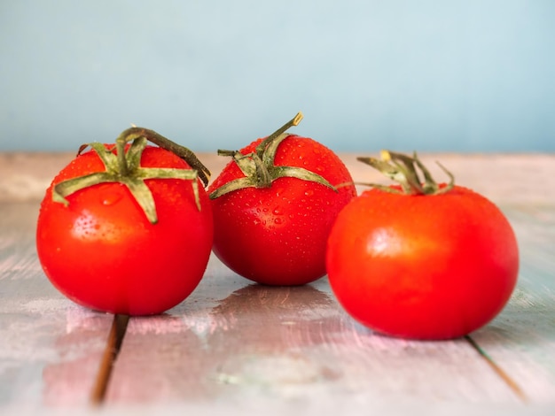 Três tomates vermelhos com folhas na mesa em close-up com foco borrado