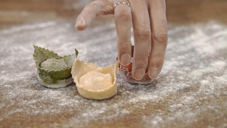 Tres tortellini crudos en una mesa de madera con una mano cerca del restaurante de la cocina