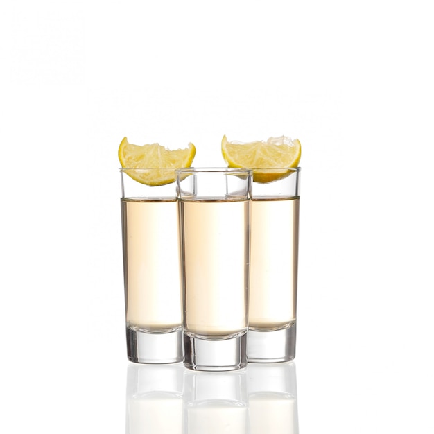 Foto tres tragos de tequila de oro con limón aislado sobre fondo blanco.