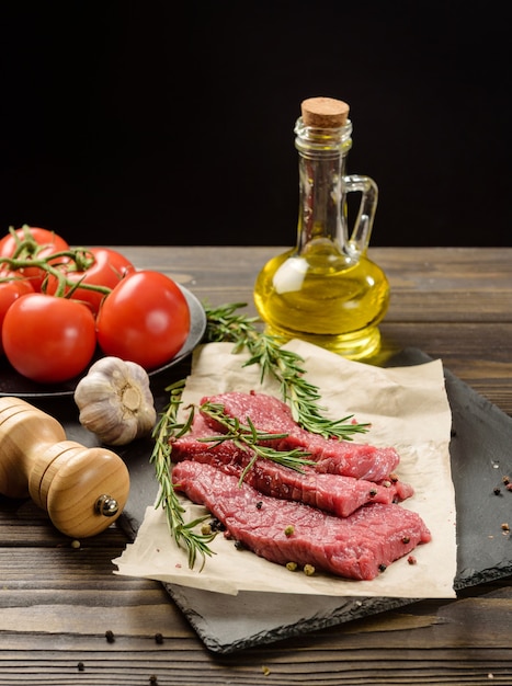 Tres trozos de carne cruda sobre una tabla para cortar. Mesa con ingredientes para cocinar bistec sobre un fondo negro.