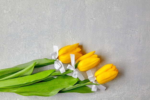 Tres tulipanes amarillos atados con lazos blancos yacen sobre una mesa de hormigón gris Vista superior con espacio de copia plano