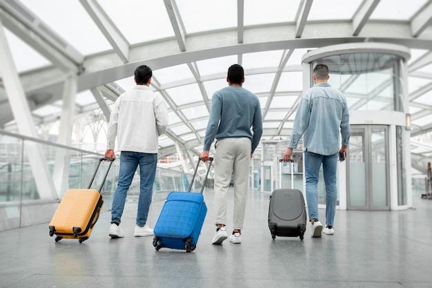 Tres turistas masculinos caminando con maletas en la vista trasera del aeropuerto