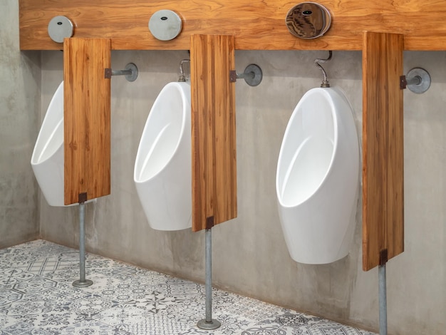 Tres urinarios automáticos blancos modernos para hombres y tabiques de madera en la pared de cemento en el baño