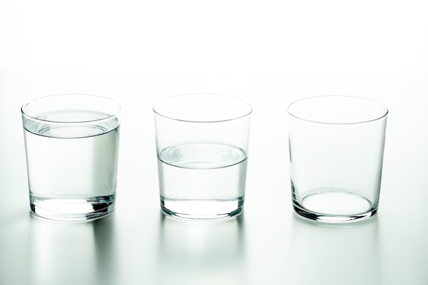 Tres vasos de cristal, uno lleno de líquido, uno medio lleno y otro vacío, concepto de cantidad y capacidad