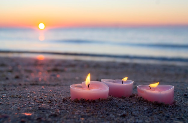 Tres velas en forma de corazón arden en la arena de la playa cerca de las olas del mar contra el backgro