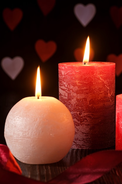 Tres velas de llama de cera con cinta en luz oscura romántica en corazones