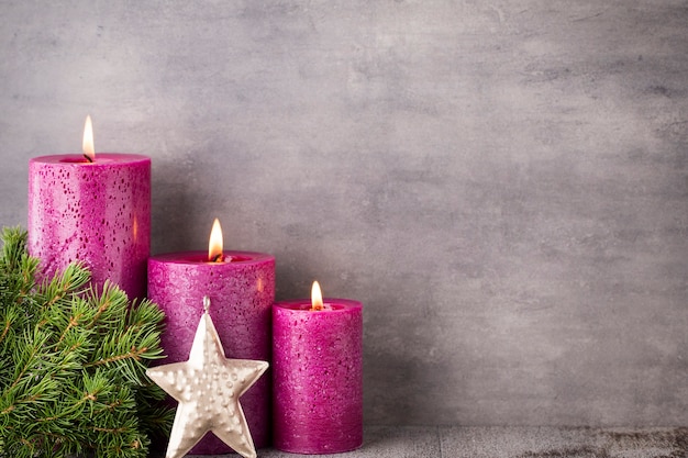 Tres velas púrpuras sobre fondo gris, decoración navideña. Estado de ánimo de Adviento.