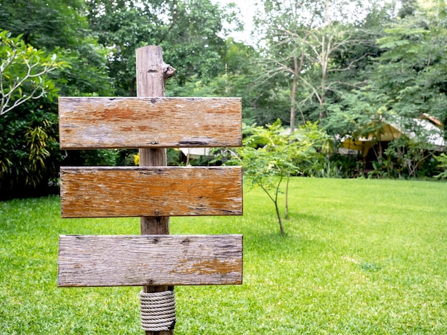 Tres viejos carteles vacíos de tablones de madera en el poste de madera cerca del jardín de hierba verde con espacio para copiar Colección de varios carteles de madera en el patio