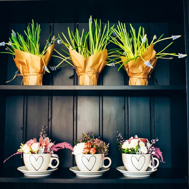 Três xícaras brancas com flores na prateleira.