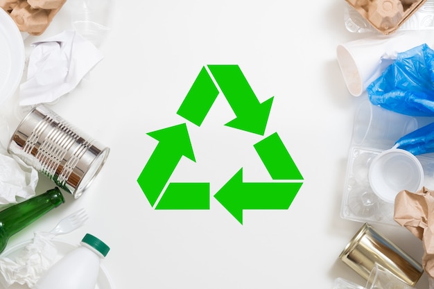 Triagem e reciclagem de resíduos. Lixo de plástico, papel, vidro e metal dispostos sobre um fundo branco. Símbolo verde no centro.