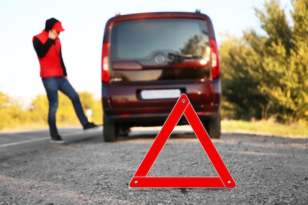 Triángulo de advertencia rojo en carretera asfaltada Conductor cerca de coche averiado