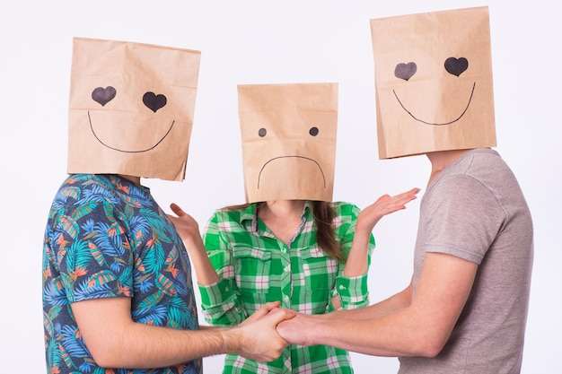 Foto triángulo amoroso, celos y concepto de homosexualidad: gays con bolsas sobre la cabeza tomados de la mano y otra mujer enojada.