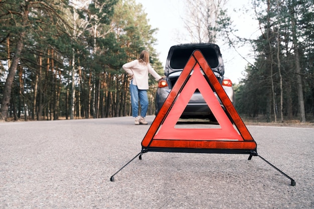 Triângulo de emergência vermelho com carro turvo e mulher chamando mecânico de carro no fundo do carro quebrado