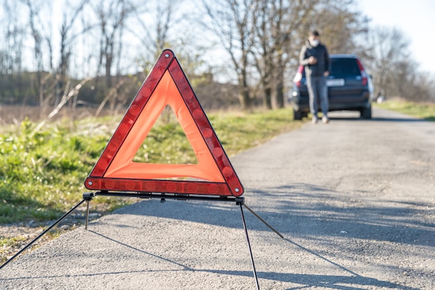 Triángulo rojo de advertencia en la carretera frente a un automóvil roto