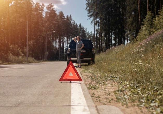 Triángulo señal de precaución en el lado de la carretera después de que el coche se avería y la conductora triste esperando la emergencia ...