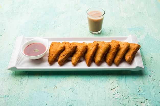 Triângulos de batata crocante ou batata vada cobertos com migalhas de pão e depois fritos. servido com ketchup de tomate. foco seletivo