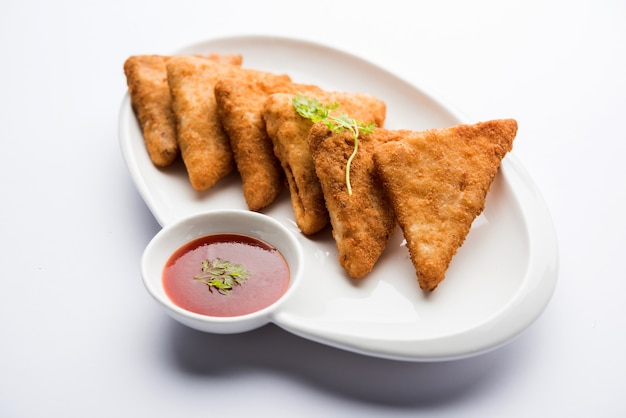 Triángulos de papa crujiente o batata vada cubiertos con pan rallado y luego fritos. servido con salsa de tomate. enfoque selectivo