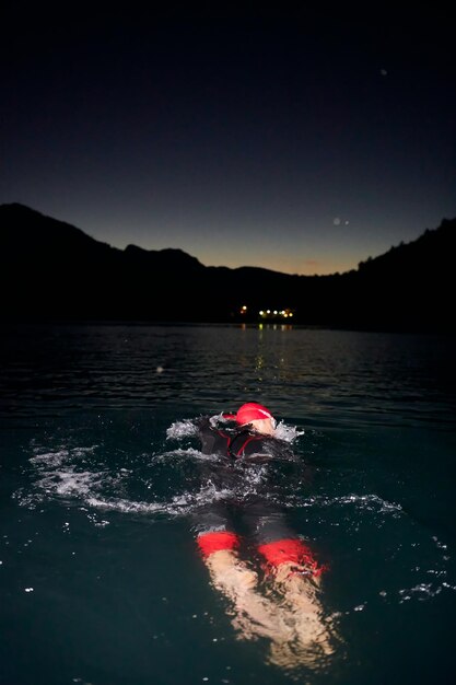 Triathlon-Athletin schwimmt in einer dunklen Nacht und trägt einen Neoprenanzug