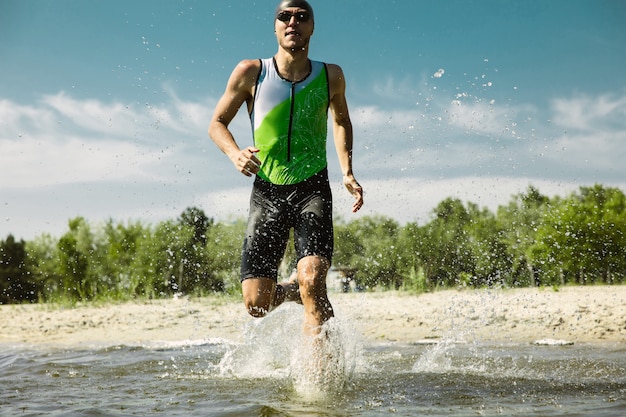 Triatleta profesional nadando en aguas abiertas de río. Hombre vestido con equipo de natación practicando triatlón en la playa en verano. Concepto de estilo de vida saludable, deporte, acción, movimiento y movimiento.