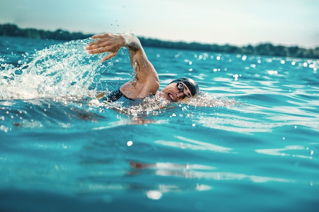 Triatleta profissional nadando em águas abertas do rio. homem usando equipamento de natação, praticando triatlo na praia em dia de verão. conceito de estilo de vida saudável, esporte, ação, movimento e movimento.