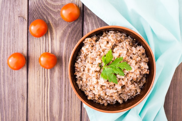 Trigo cozido em uma tigela com uma folha de salsa e tomate cereja em uma mesa de madeira, vista superior