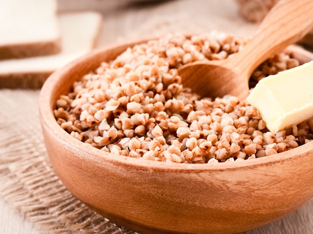 Trigo sarraceno cozido em uma placa de madeira com uma colher e um close-up de manteiga. Fundo alimentar