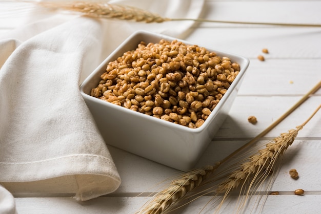 Trigo tostado crujiente - Suplemento dietético indio, servido en un recipiente blanco sobre fondo cambiante, enfoque selectivo