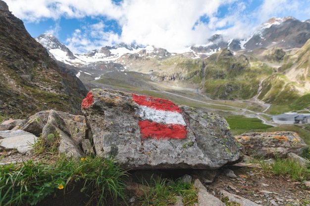 Trilha alpina na Áustria, marcada com uma bandeira austríaca pintada em uma rocha ao longo da rota.