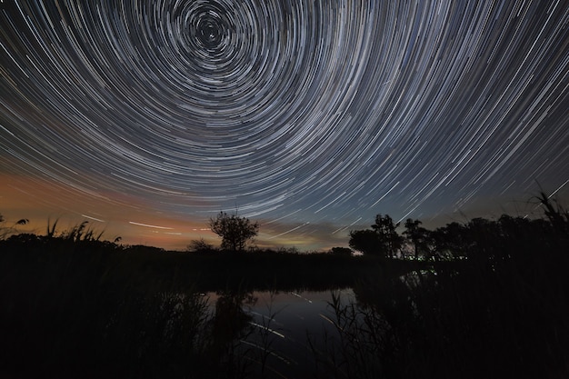 Trilha de estrelas no céu noturno com nuvens refletidas no rio