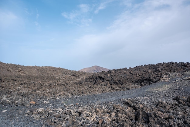 Trilha entre lava com vista para o vulcão Caldera Blanca Timanfaya Ilhas Canárias Lanzarote Espanha