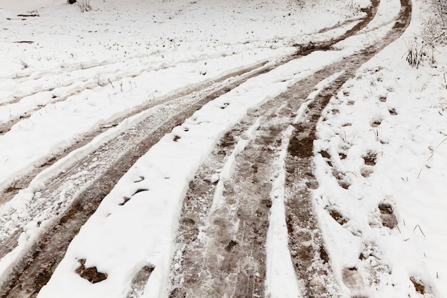 Trilhas das rodas do carro em uma estrada rural coberta de neve não pavimentada. Na neve, há pegadas.