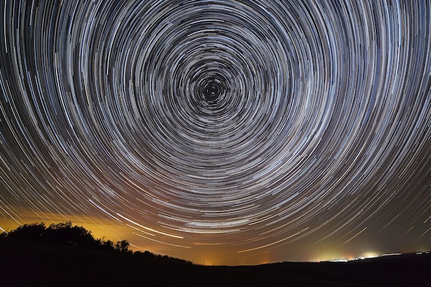 Trilhas de estrelas no céu noturno. Uma vista do espaço estrelado e da luz acima do horizonte.