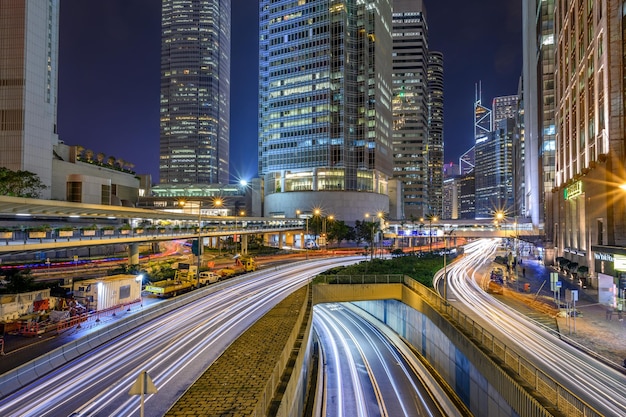 Trilhas de luz na estrada em meio a edifícios na cidade à noite