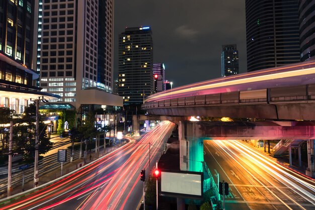 Trilhas de luz na estrada em meio a edifícios na cidade à noite