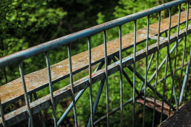 Trilho de guarda de metal antigo da ponte, com floresta verde turva no fundo.