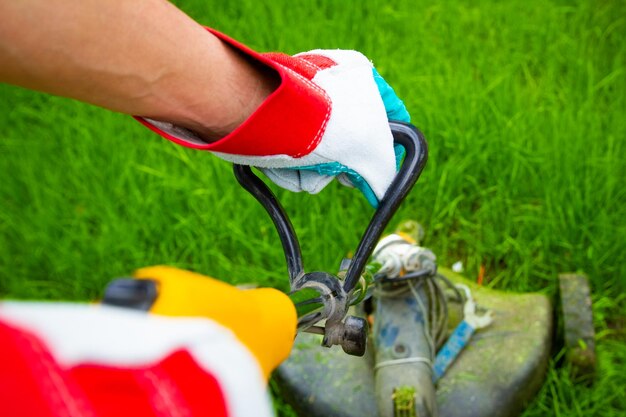 Un trímero de hombre corta la hierba en el campo en el fondo del parque