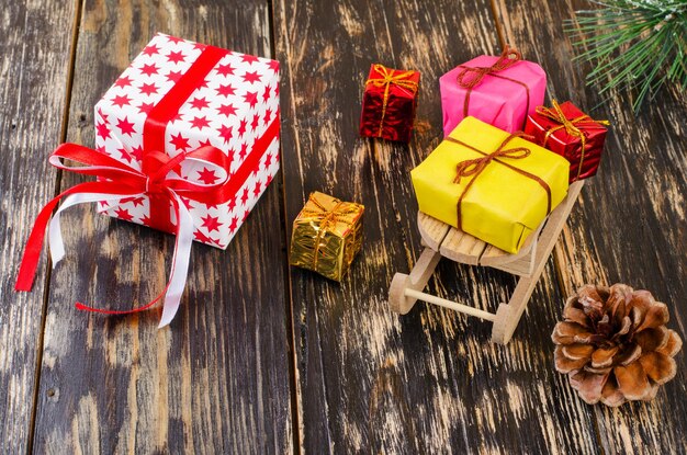 Foto el trineo de navidad con regalos están en un fondo oscuro cerca de los regalos de mentira cono de pino y rama de abeto