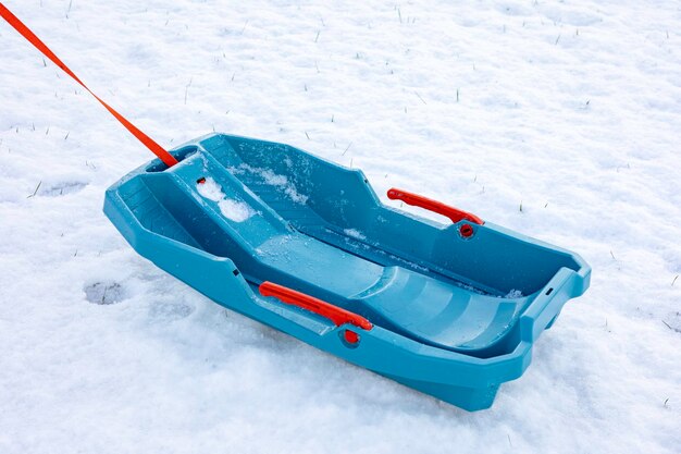 El trineo de plástico azul vacío con una cuerda roja se encuentra en un espacio de tierra cubierto de nieve para el texto