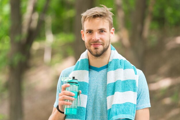 Trinken Sie etwas Wasser Man Jogger mit Handtuch auf den Schultern hält Wasserflasche Man Athlet Sportkleidung erfrischend Sport und gesundes Lifestyle-Konzept Athlet trinkt Wasser nach dem Training im Park