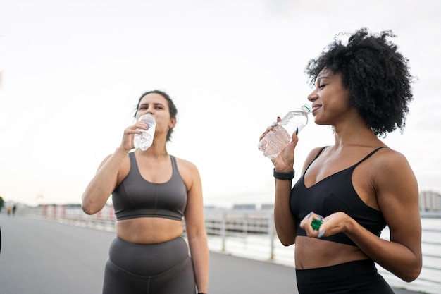 Trinken Sie Wasser aus einer Flasche. Pause, Sportler, Freunde, Frauen, Ruhe, Freunde, Training, Fitness, Laufen