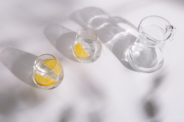 Trinken von natürlichem Wasser in schönen Gläsern mit Zitronenscheibe auf weißem Hintergrund am sonnigen Tag