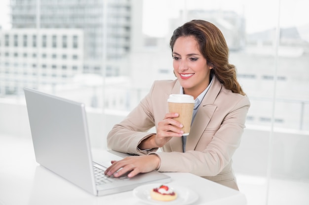 Trinkender Kaffee der Geschäftsfrau an ihrem Schreibtisch unter Verwendung des Laptops