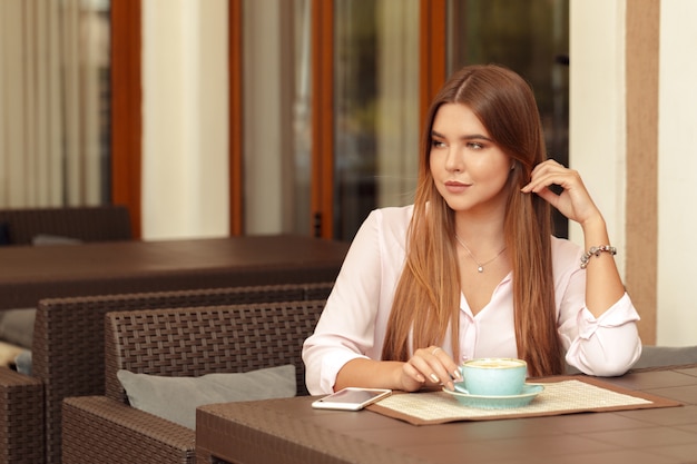 Trinkender Kaffee der jungen Frau in einem Café draußen