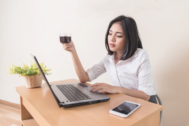 Trinkender Kaffee der jungen Geschäftsfrau beim Arbeiten mit Laptop am Schreibtisch.
