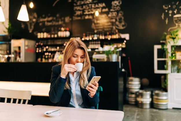 Trinkender Kaffee der Schönheit und Telefon im Restaurant verwenden.