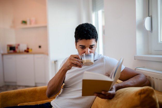 Trinkender Kaffee des Afroamerikanermannes und ein Buch zu Hause lesen.