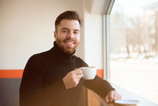 Trinkender Kaffee des attraktiven erfolgreichen jungen Geschäftsmannes, der am Cafétisch sitzt.