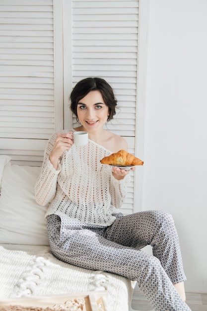 Trinkender Kaffee und ein Hörnchen des Mädchens im Bett