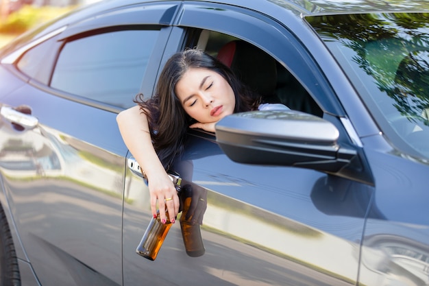 Trinkendes Bier der jungen asiatischen Frau beim Autofahren.